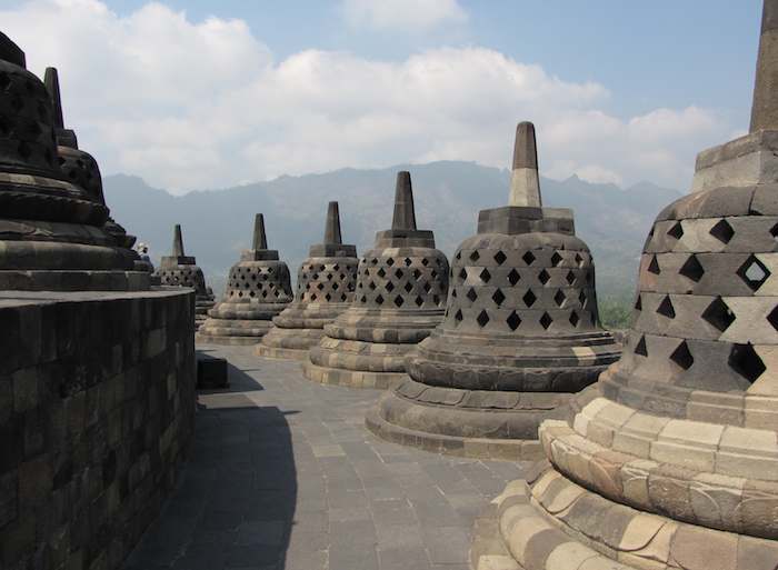 photo of stupas at Borobudur Buddhist temple with mountains in the background