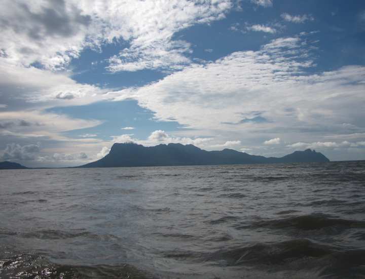 photo of sea with island in the background and clouds dotting a blue sky