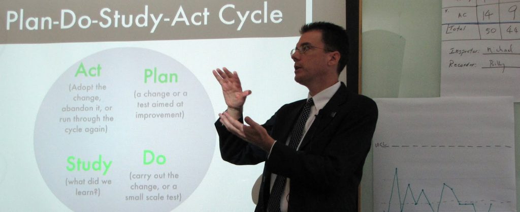 photo of John Hunter in front of graphic for Plan Do Study Act cycle